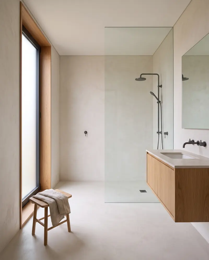 Mikro çimento kaplı banyo. Cam bölmeli duş, meşe lavabo dolabı ve buzlu camlı dikey pencere. Temsili görselleştirme.